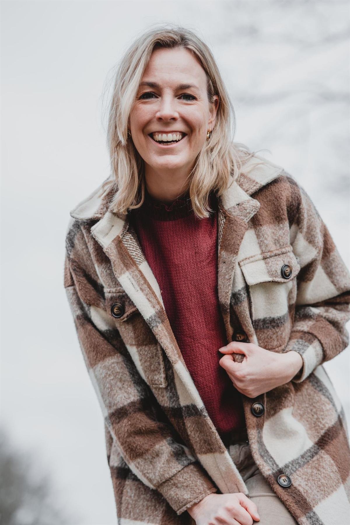 Portret van Yanieke Nijenkamp, lachend in een geruite jas.