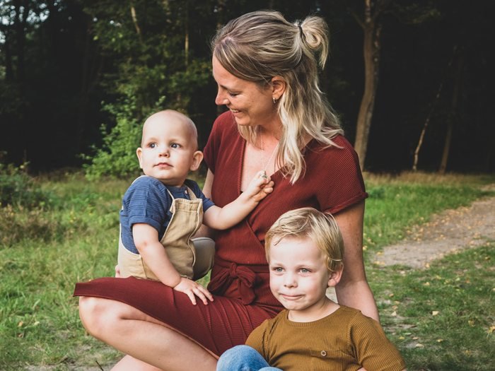 Een moeder zit op een bospad met haar twee jonge kinderen bij zich.